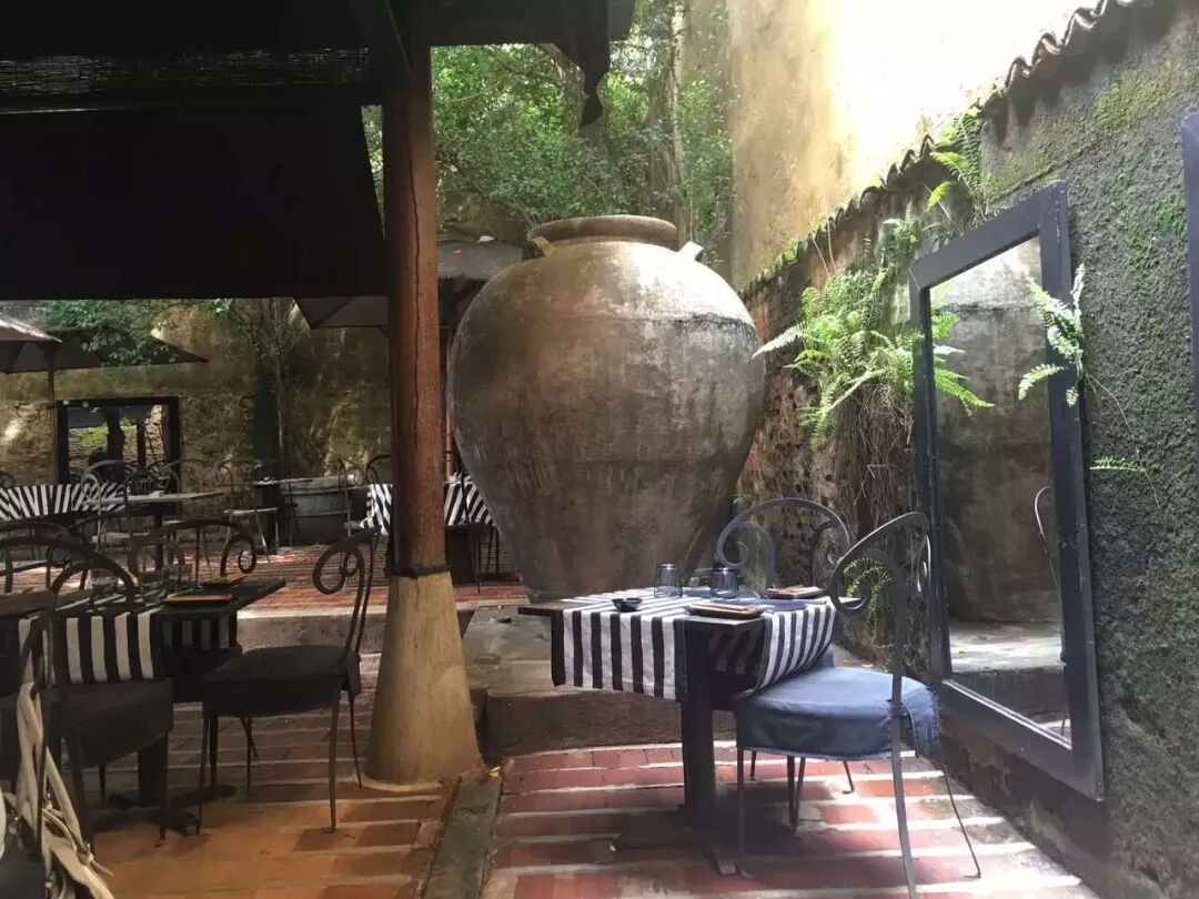 A sheltered dining space with plants and a large ceramic vessel.